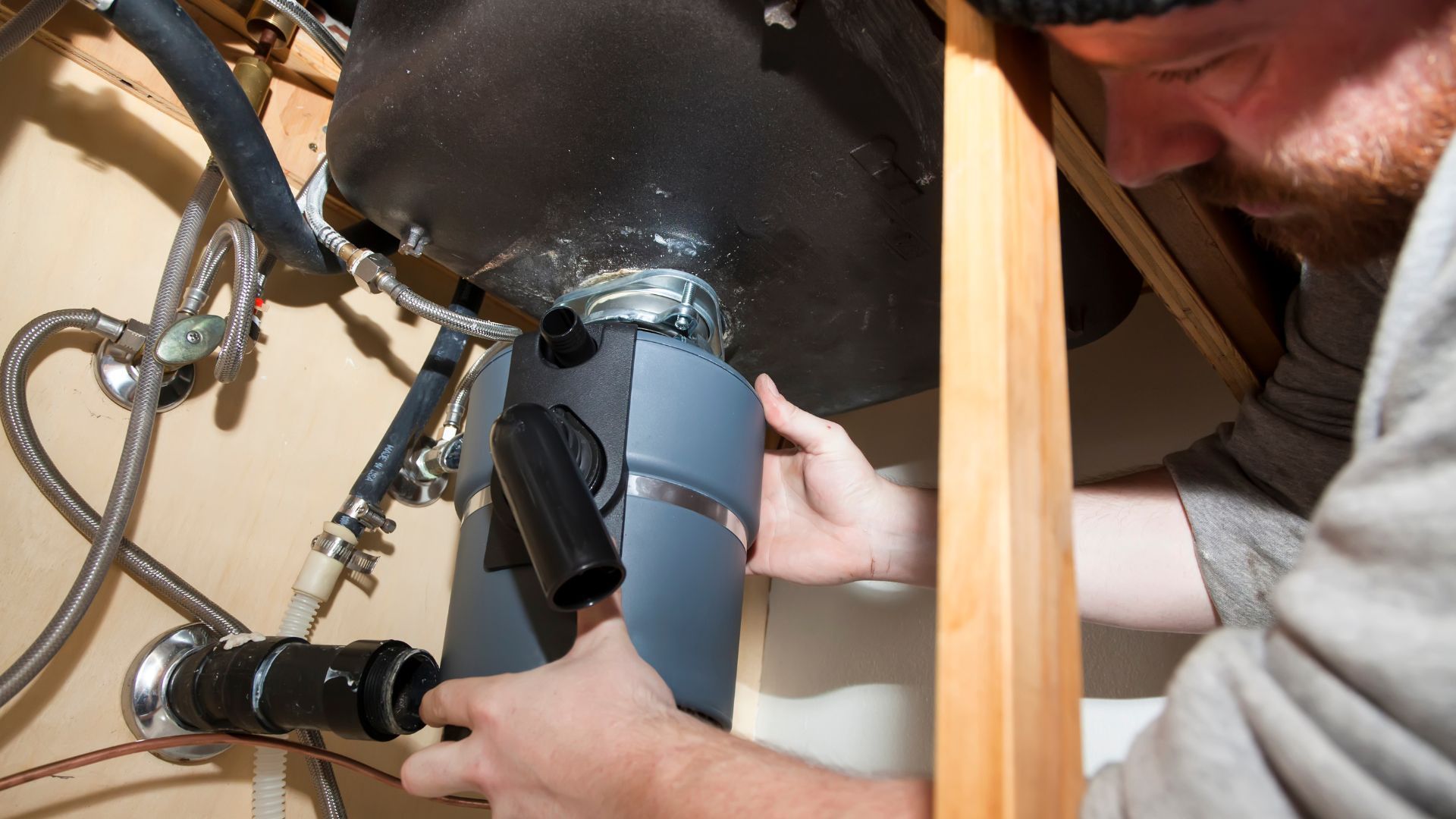 A man is fixing a pipe under a sink in a kitchen.