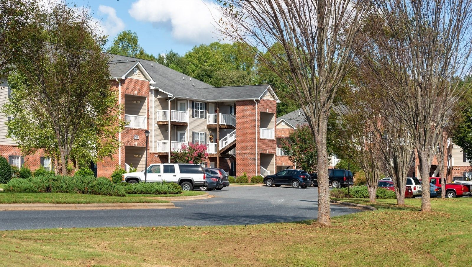 Apartment building with brick accents and parked cars on a sunny day.