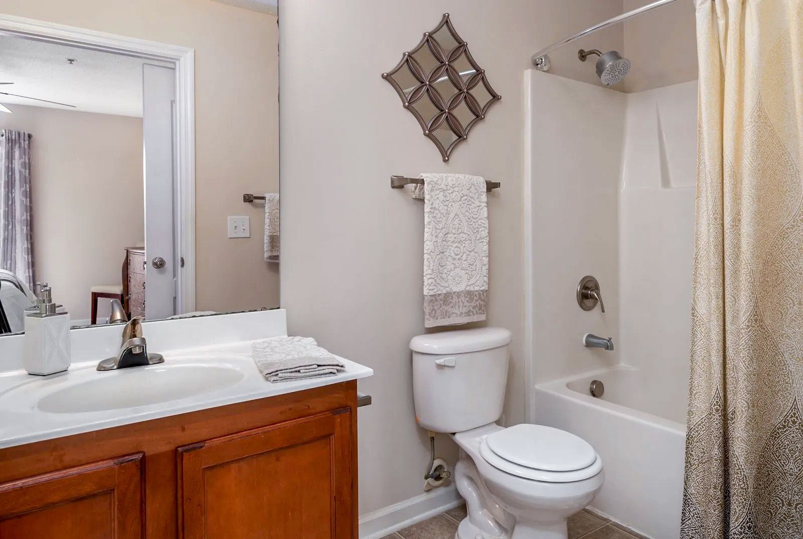 Bathroom with vanity, toilet, and shower/tub. Beige walls, wood vanity, mirror, and decorative wall art.