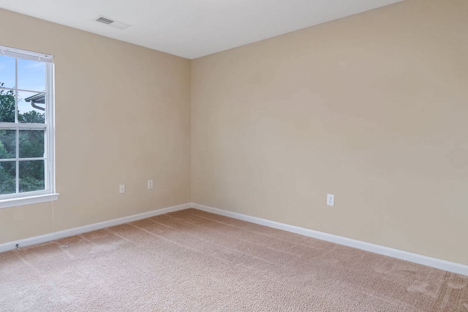 Empty beige room with a window, tan carpet, and beige walls.