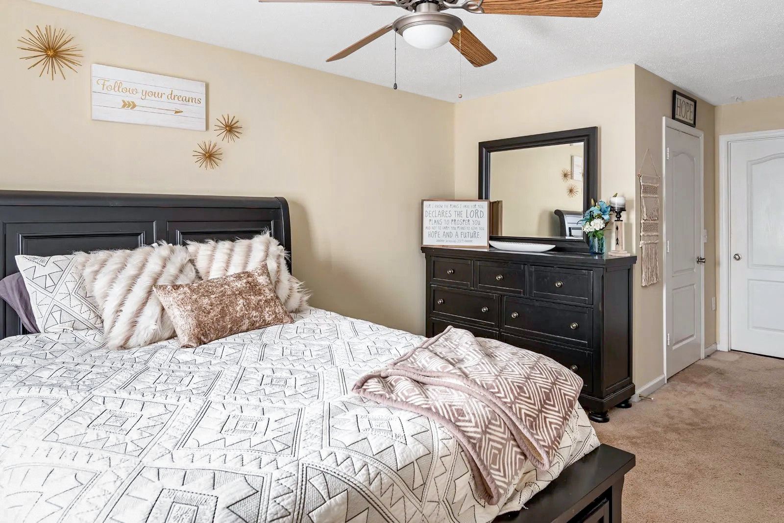 Bedroom with bed, dresser, mirror, and ceiling fan. Neutral color scheme, decorative accents.