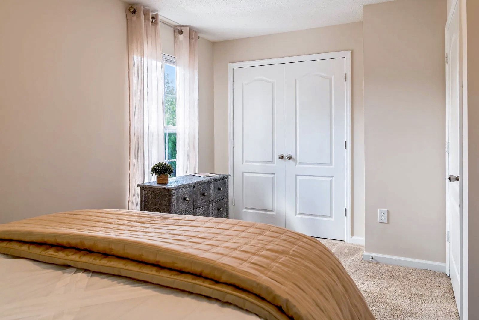 Bedroom with bed, chest, window with sheer curtain, and white double doors.