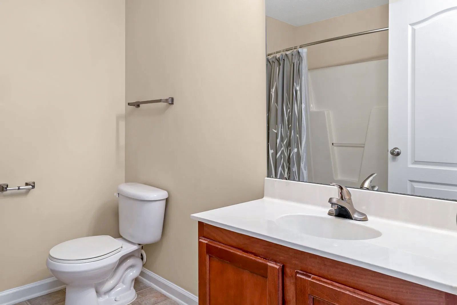 Bathroom with toilet, sink, mirror, and shower, light tan walls, and a wooden vanity.