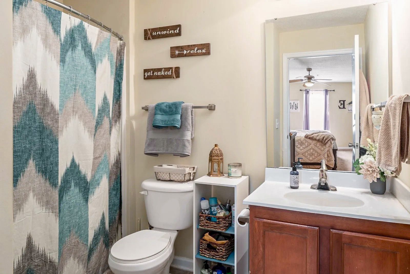 Bathroom with patterned shower curtain, toilet, vanity, and decorative accents in neutral tones.
