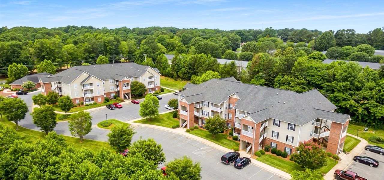 Aerial view of apartment buildings surrounded by lush green trees and a parking lot.