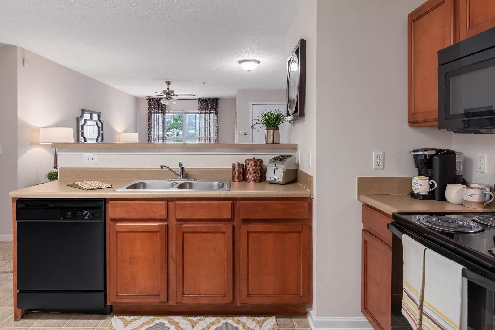 Kitchen with brown cabinets, black appliances, and countertop with partial wall view into the living space.
