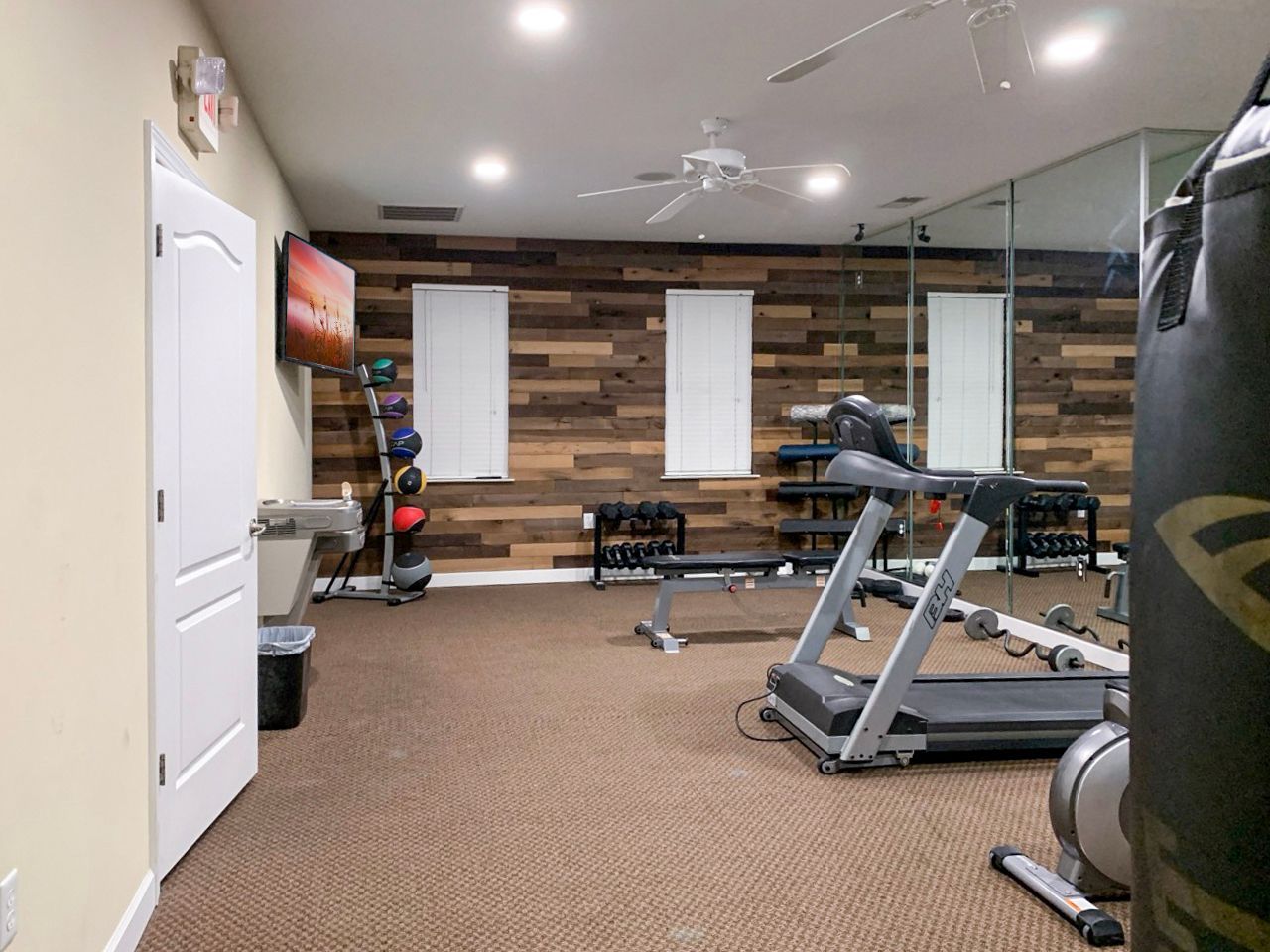 Home gym with various equipment: treadmill, weights, punching bag, and wood accent wall.