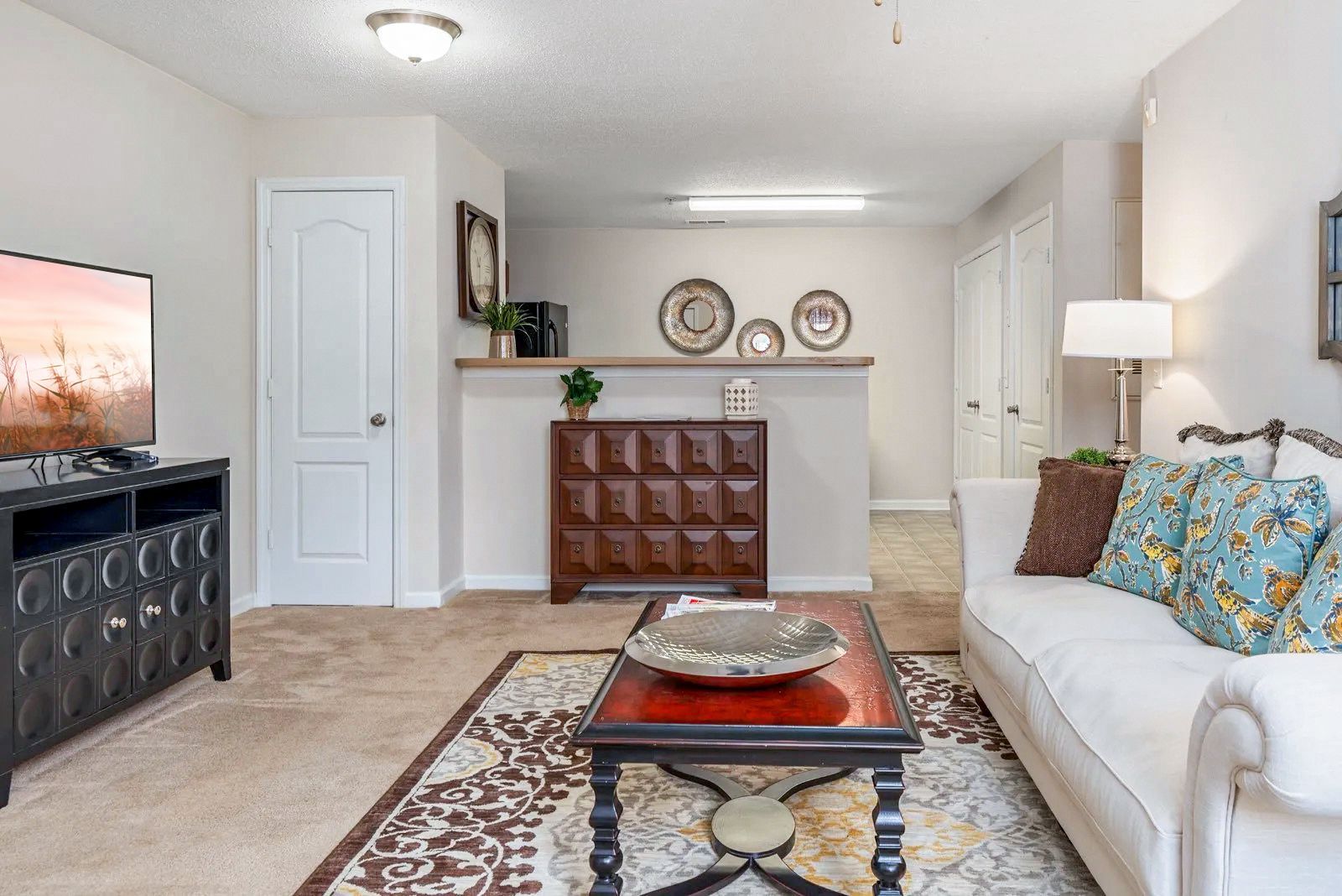 Living room with TV, white sofa, brown coffee table, and decorative wall art.