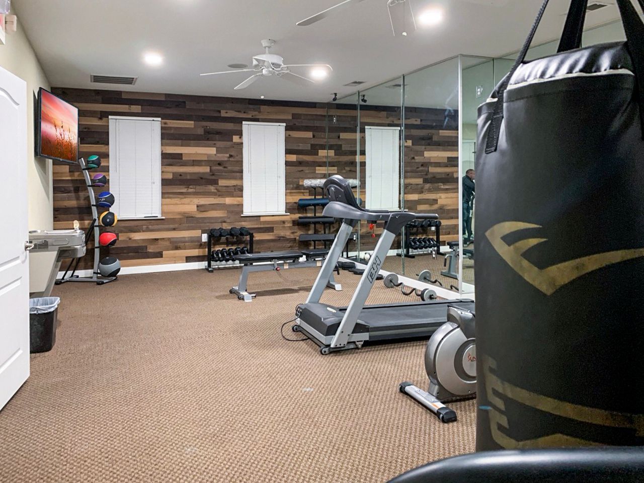 Home gym with wood accent wall, exercise equipment, mirror, and punching bag.