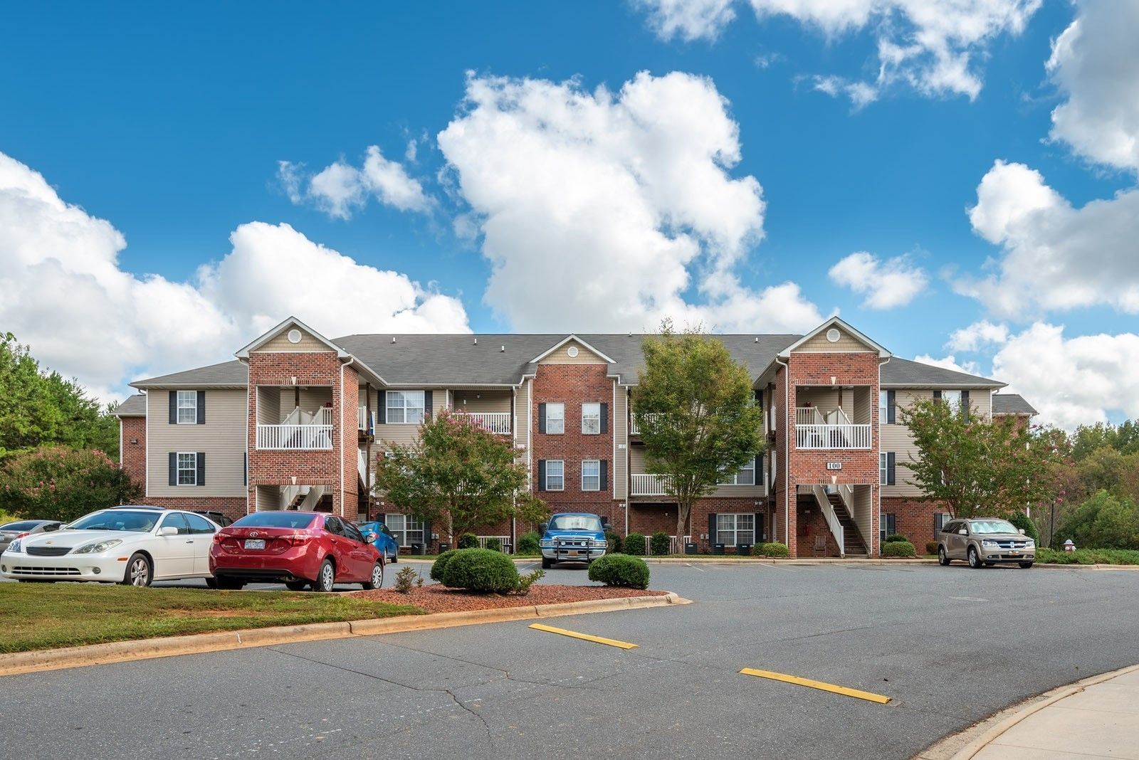 Apartment building exterior with cars parked in front, under a blue sky with clouds.