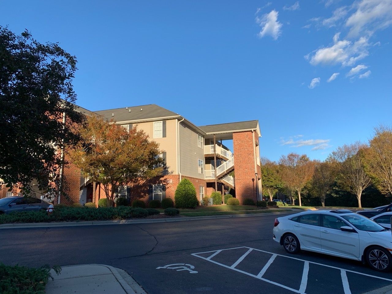 Apartment building with brick and siding, trees, blue sky, and parked cars.