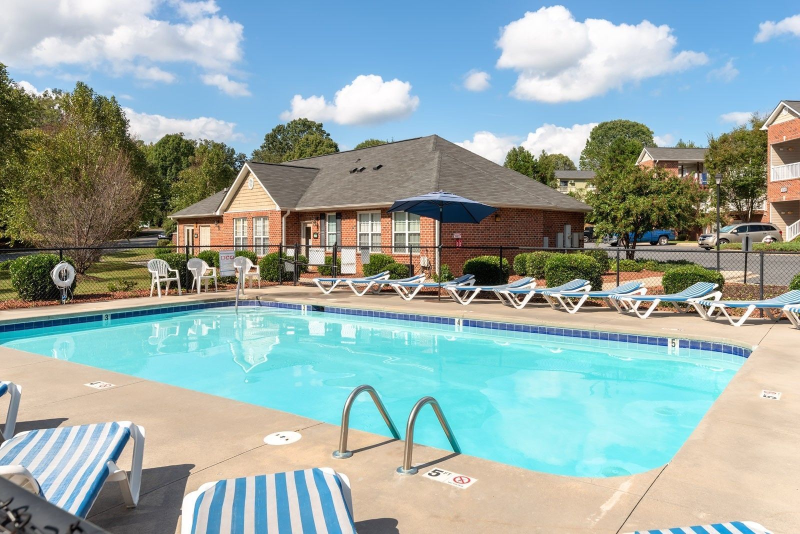 Swimming pool with lounge chairs, umbrella, and a building under a blue sky.