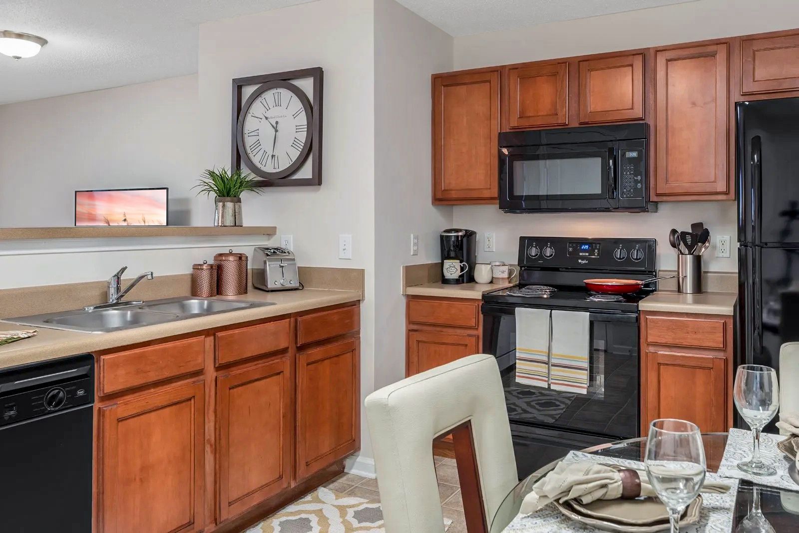 Kitchen with brown cabinets, black appliances, a round clock, and a dining table set.