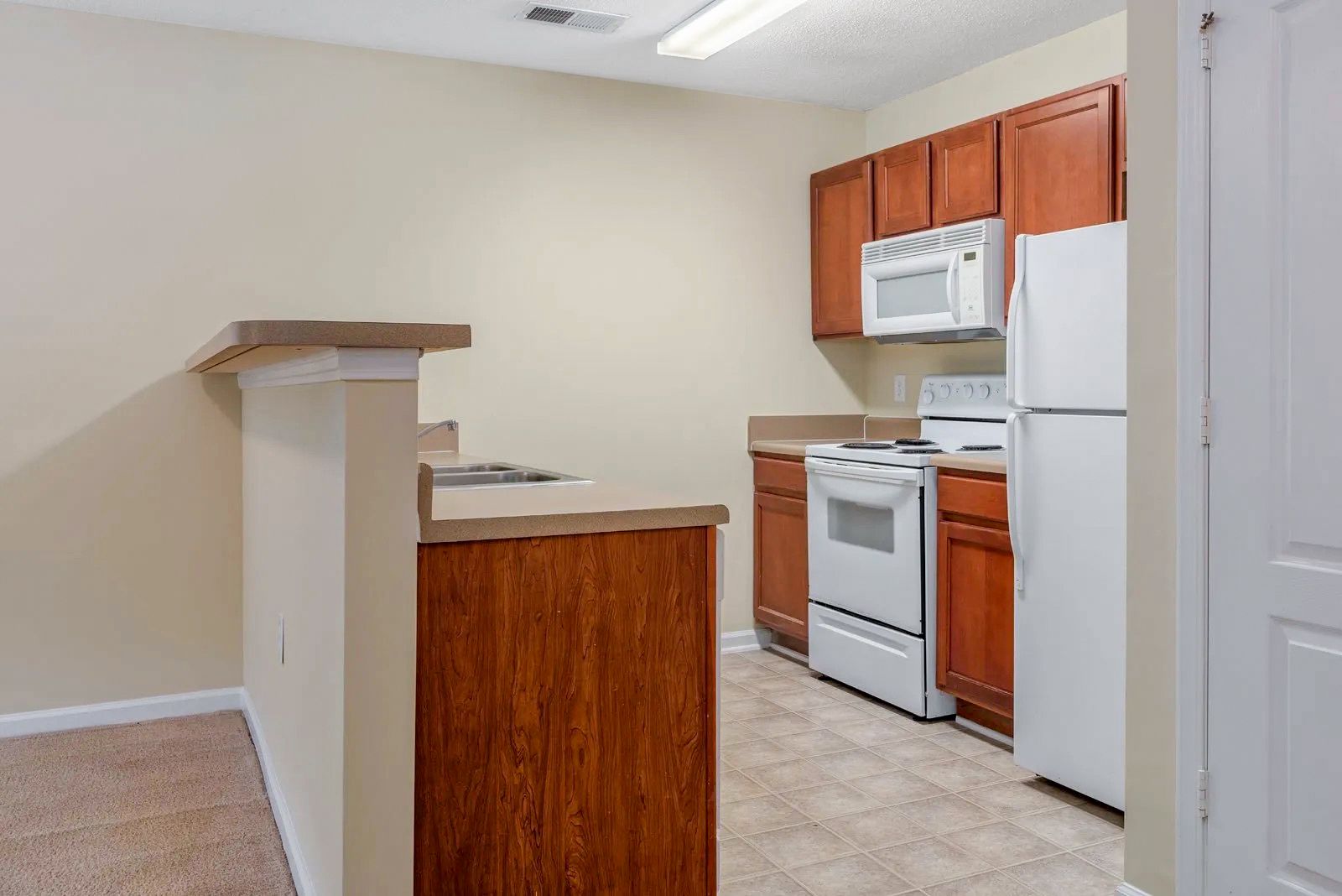Kitchen with brown cabinets, white appliances, beige countertop, and light-colored flooring.