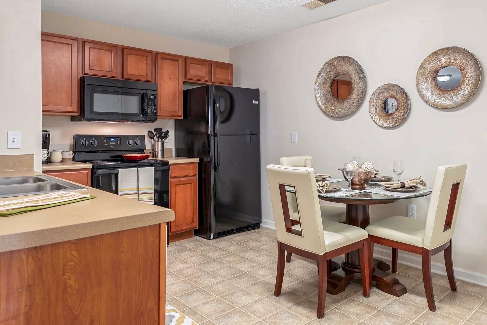 Kitchen with wooden cabinets, black appliances, and a small dining table with three chairs.