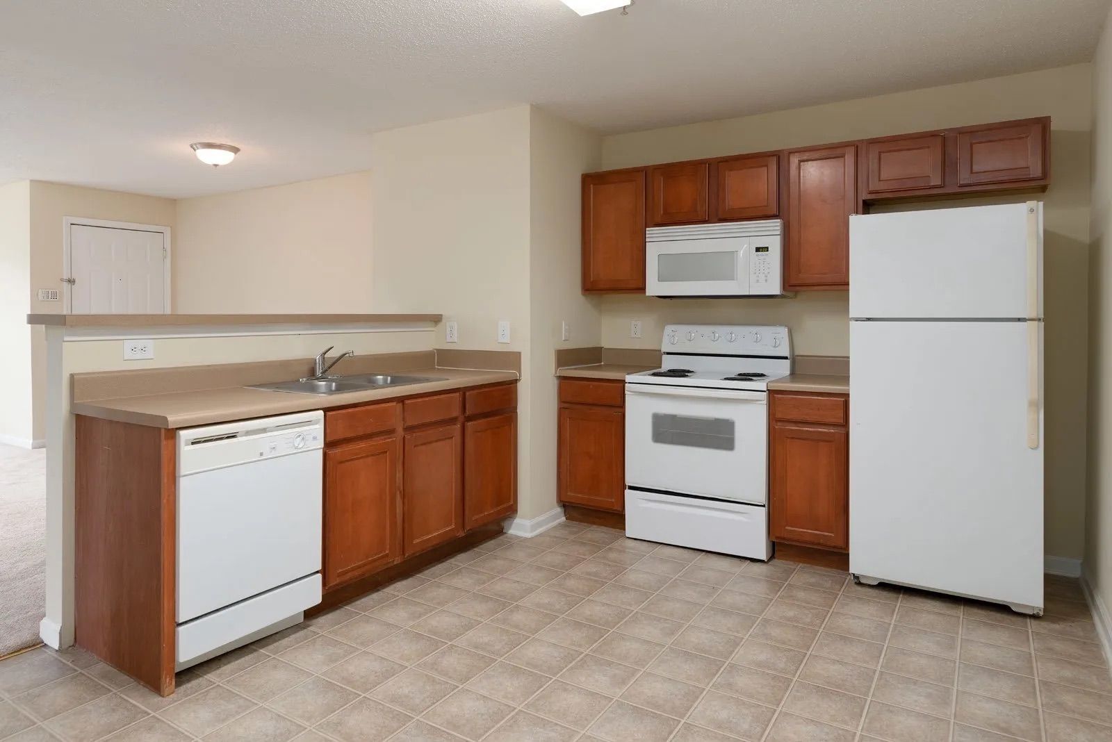 Kitchen with white appliances, brown cabinets, beige countertop, and flooring.