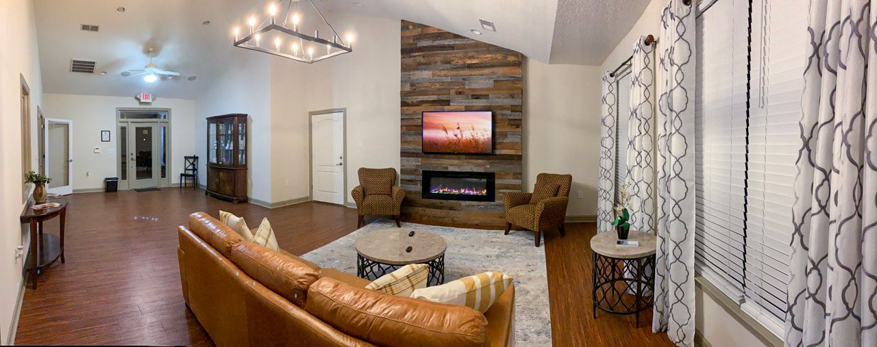 Spacious living room with fireplace, brown leather sofa, and large windows with patterned curtains.