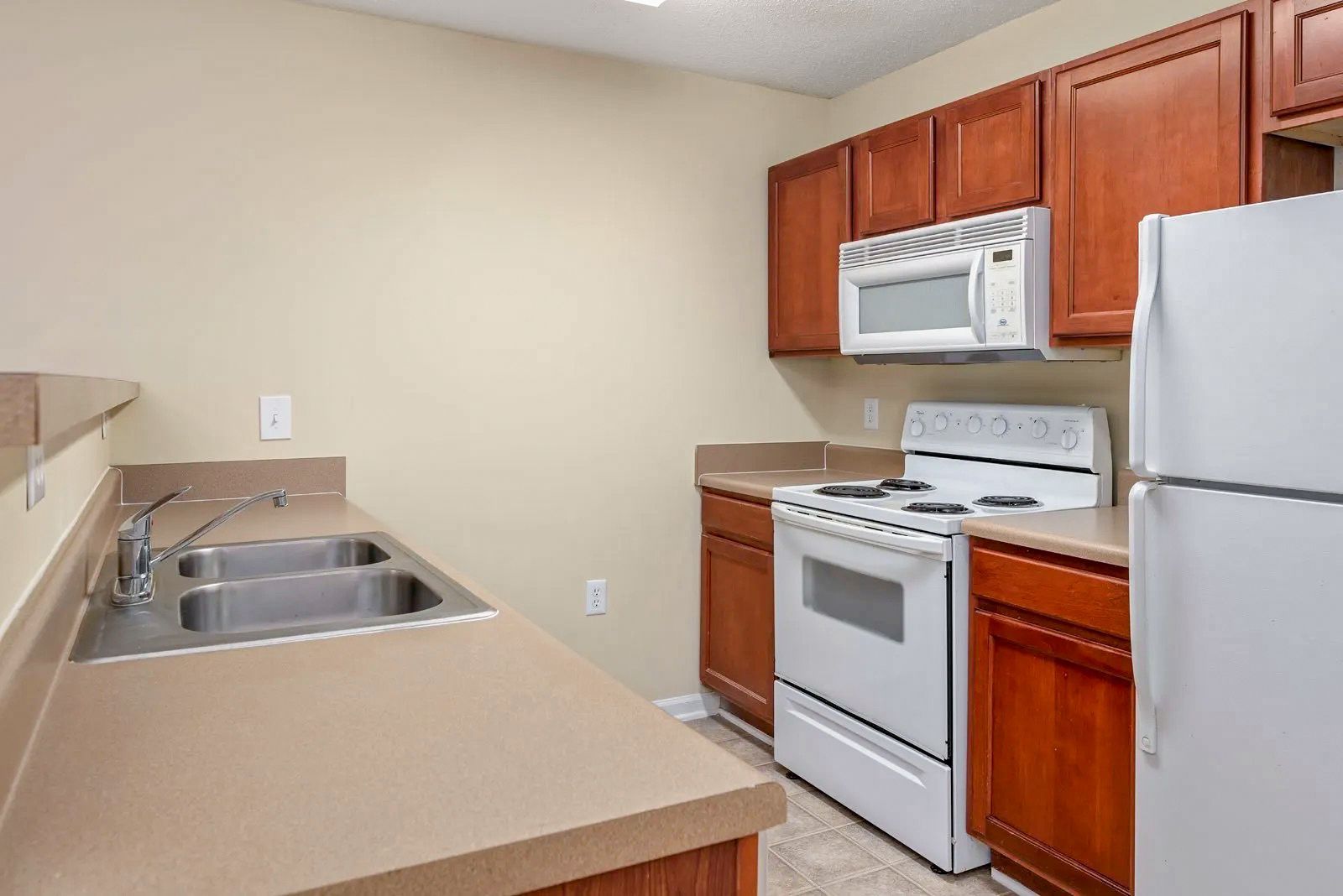 Kitchen with white appliances, brown cabinets, tan countertops, and a double sink.