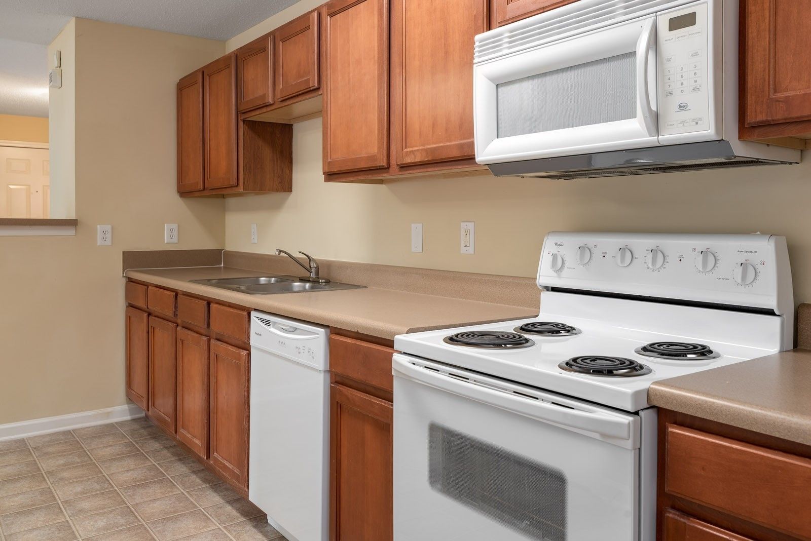 Kitchen with wooden cabinets, white appliances, and beige countertops and walls.