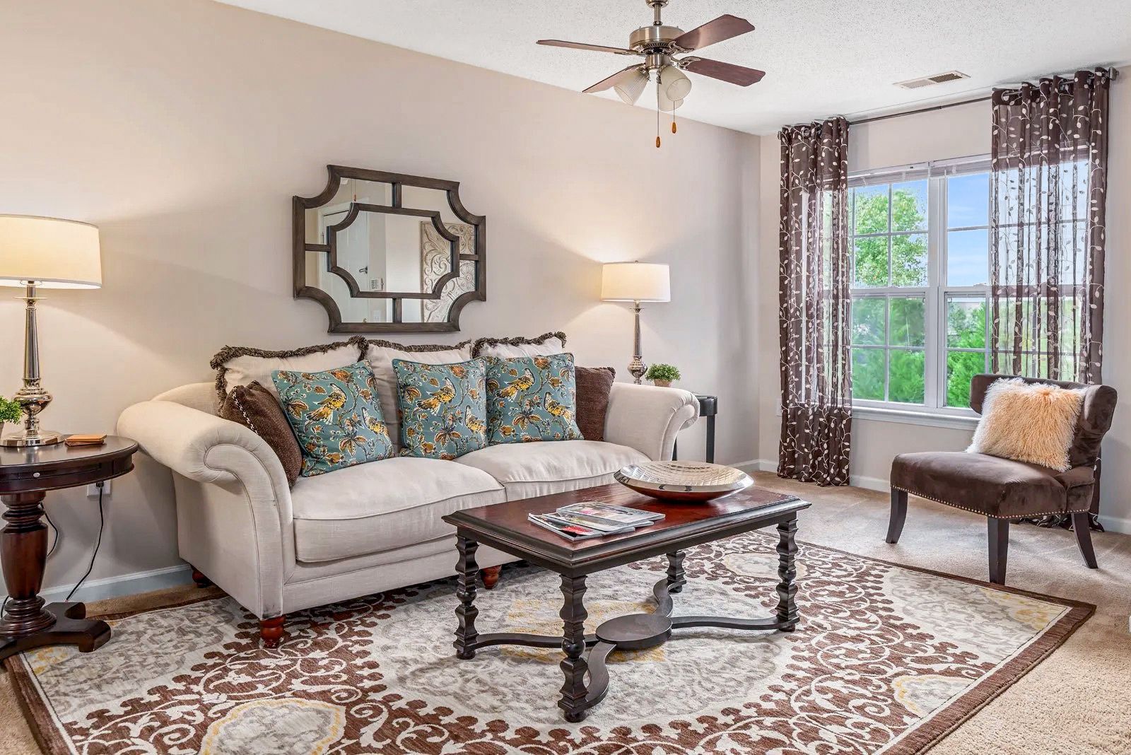 Living room with a sofa, coffee table, and patterned rug. A mirror hangs above the sofa.