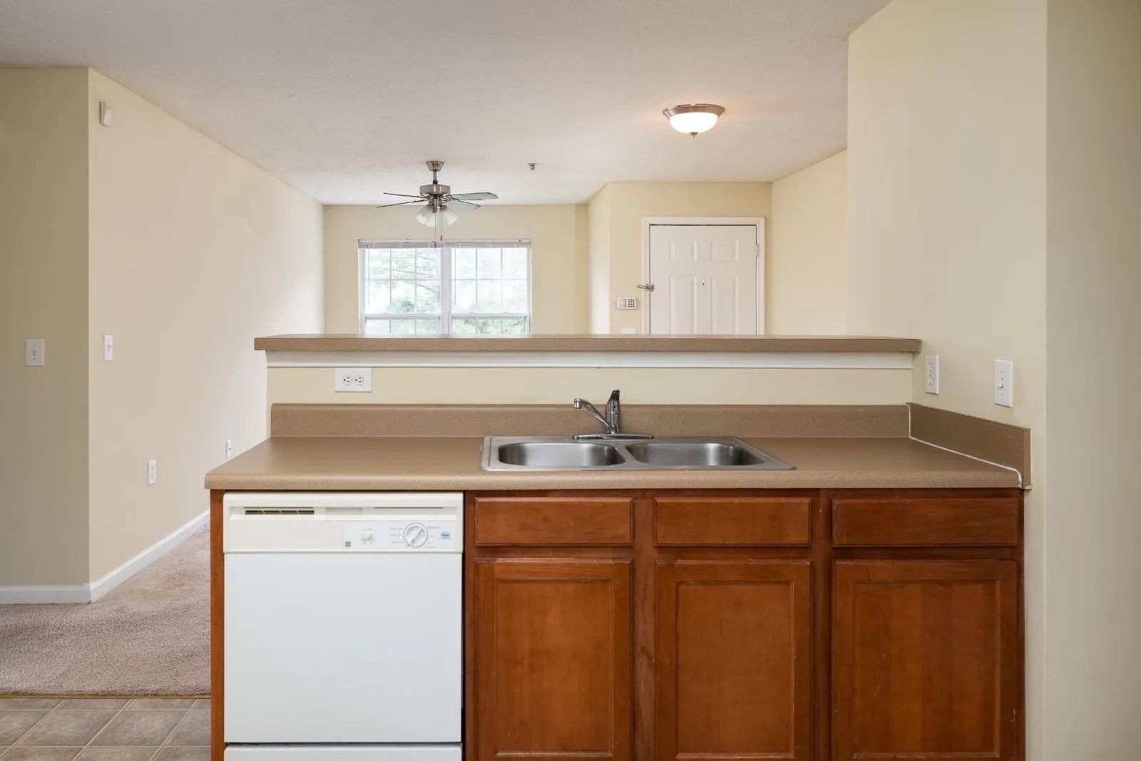 Kitchen with a sink, dishwasher, and cabinets. Beige walls, brown countertops, and view to living area.
