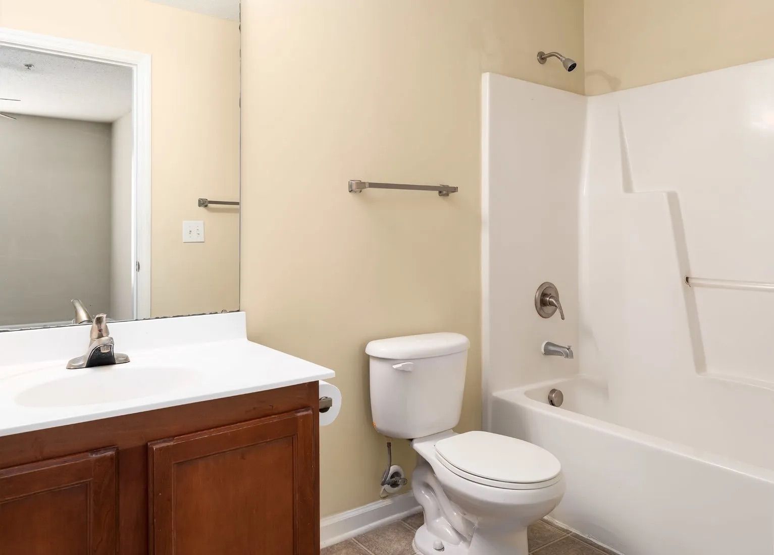 Bathroom with white bathtub, toilet, sink, mirror, and beige walls.