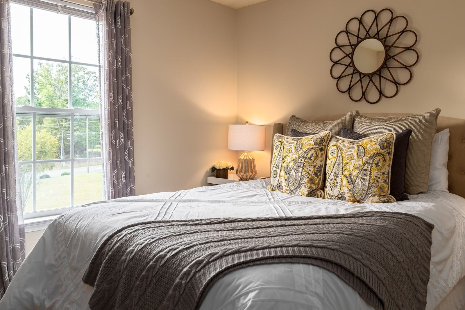 Bedroom with a bed, window, nightstand with lamp, and a decorative mirror.