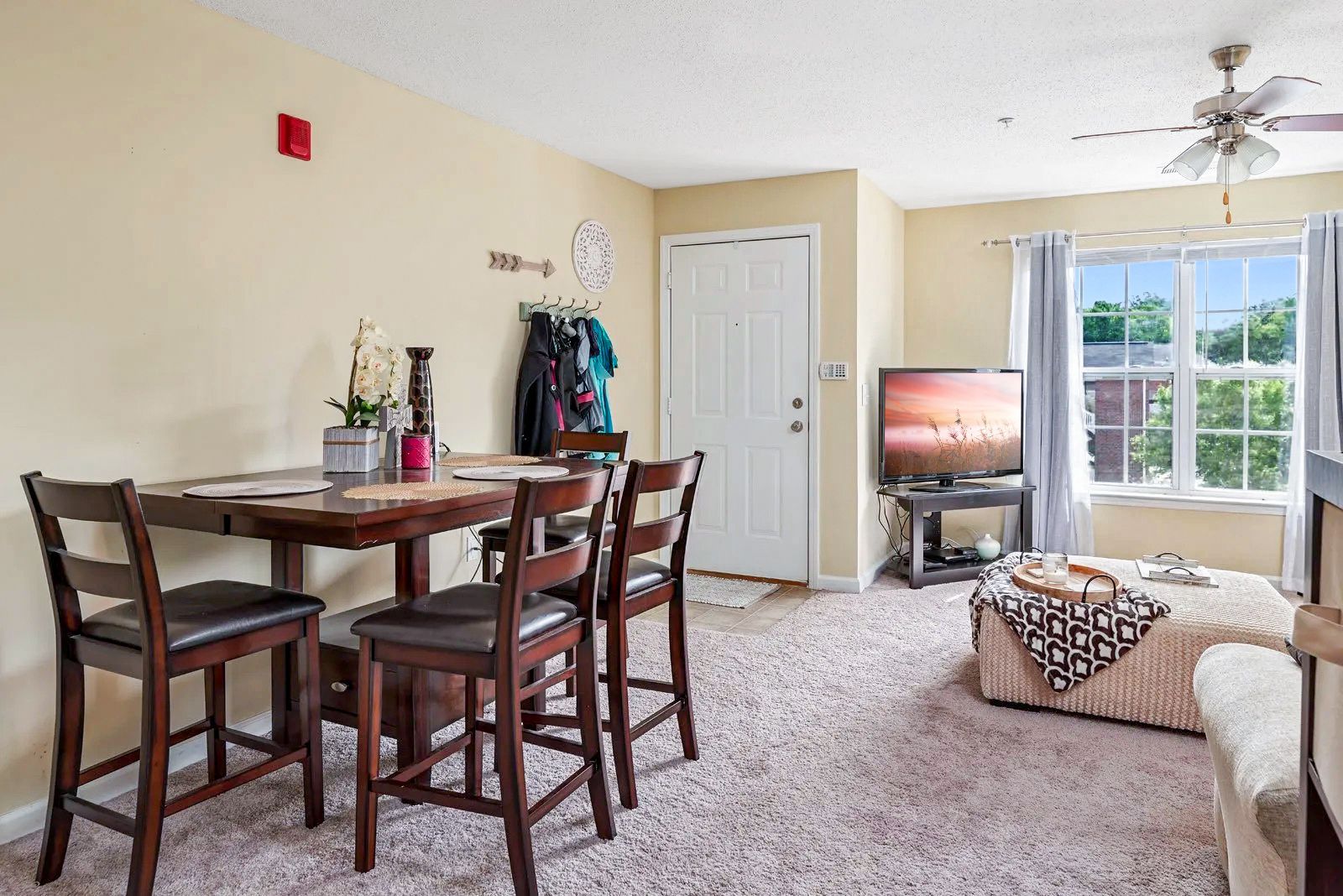 Dining area with square table, chairs, and living room with TV and window.