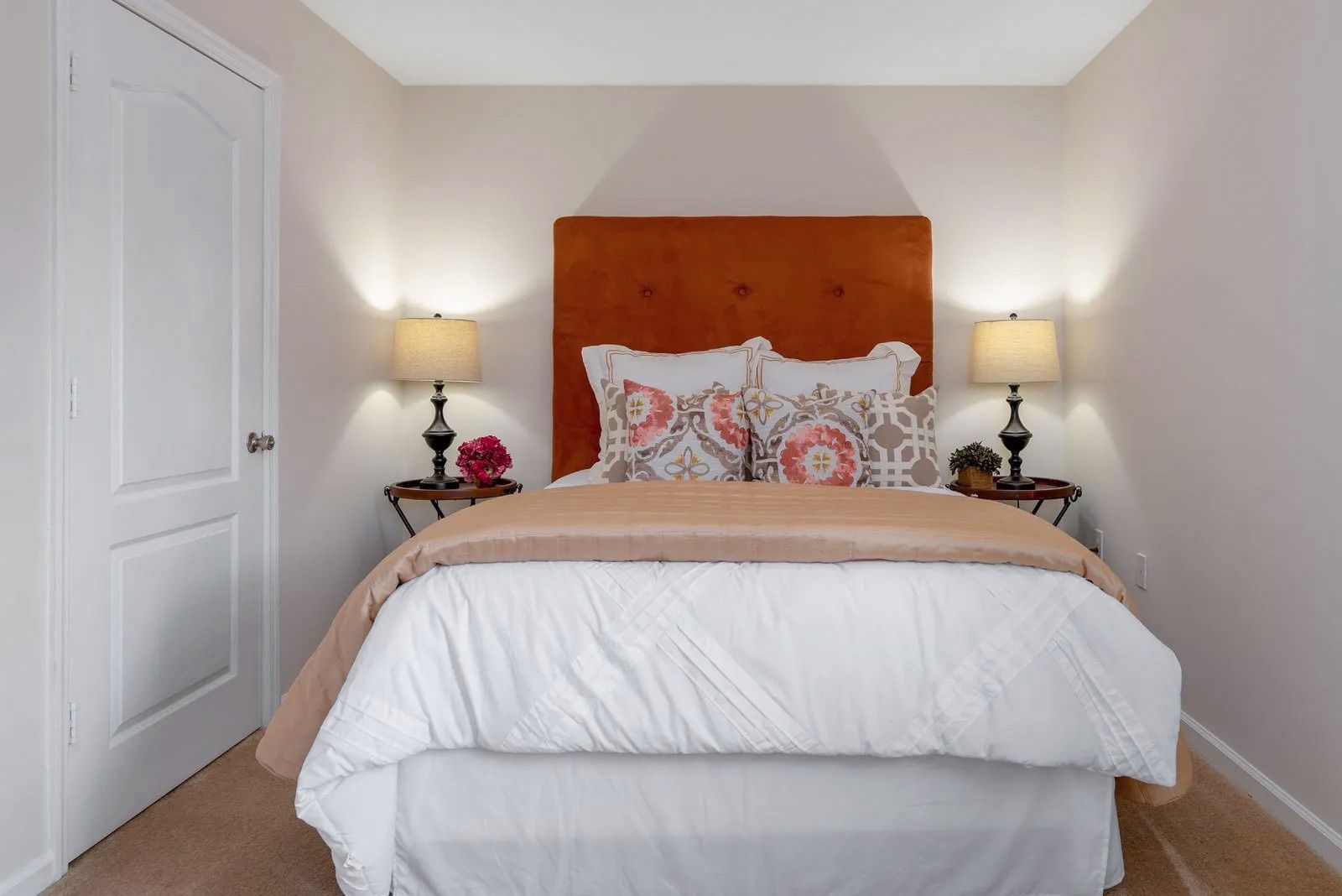 Bedroom with orange headboard, two lamps, and small bedside tables. White bedding and light walls.