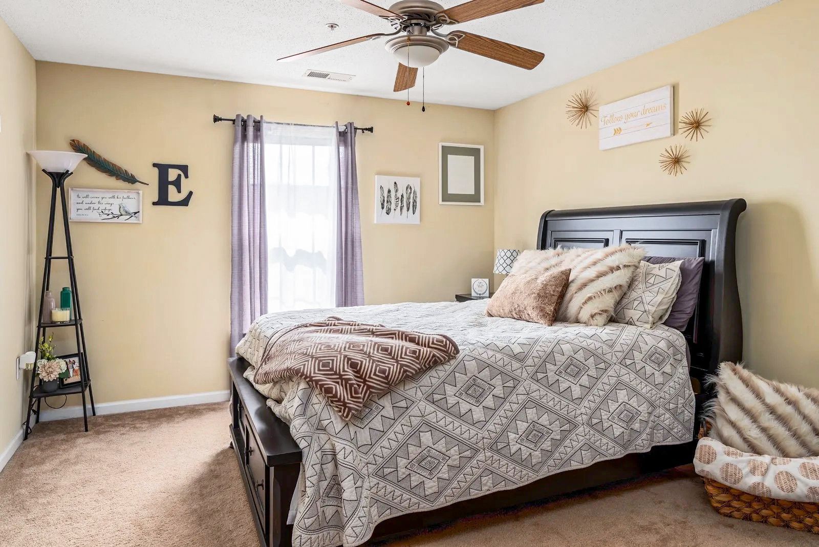 Bedroom with bed, lamp, window with purple curtains, and decorative items on the walls.