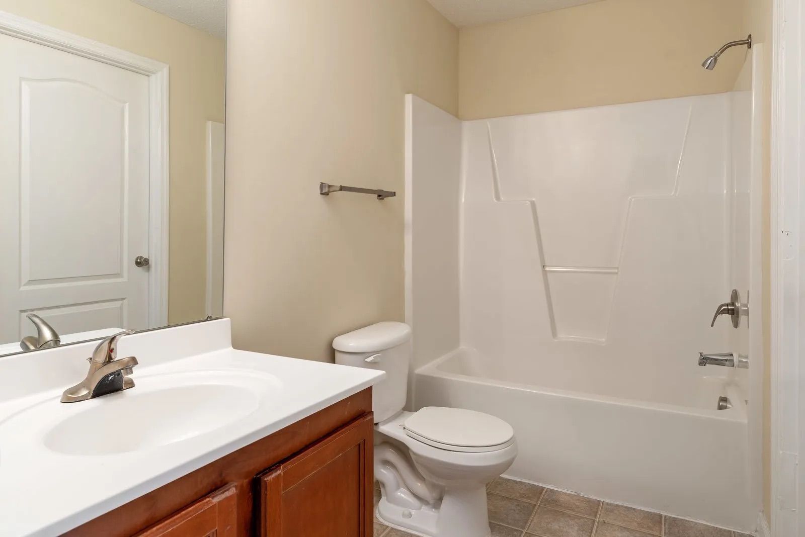 Bathroom with white fixtures, beige walls, brown vanity.
