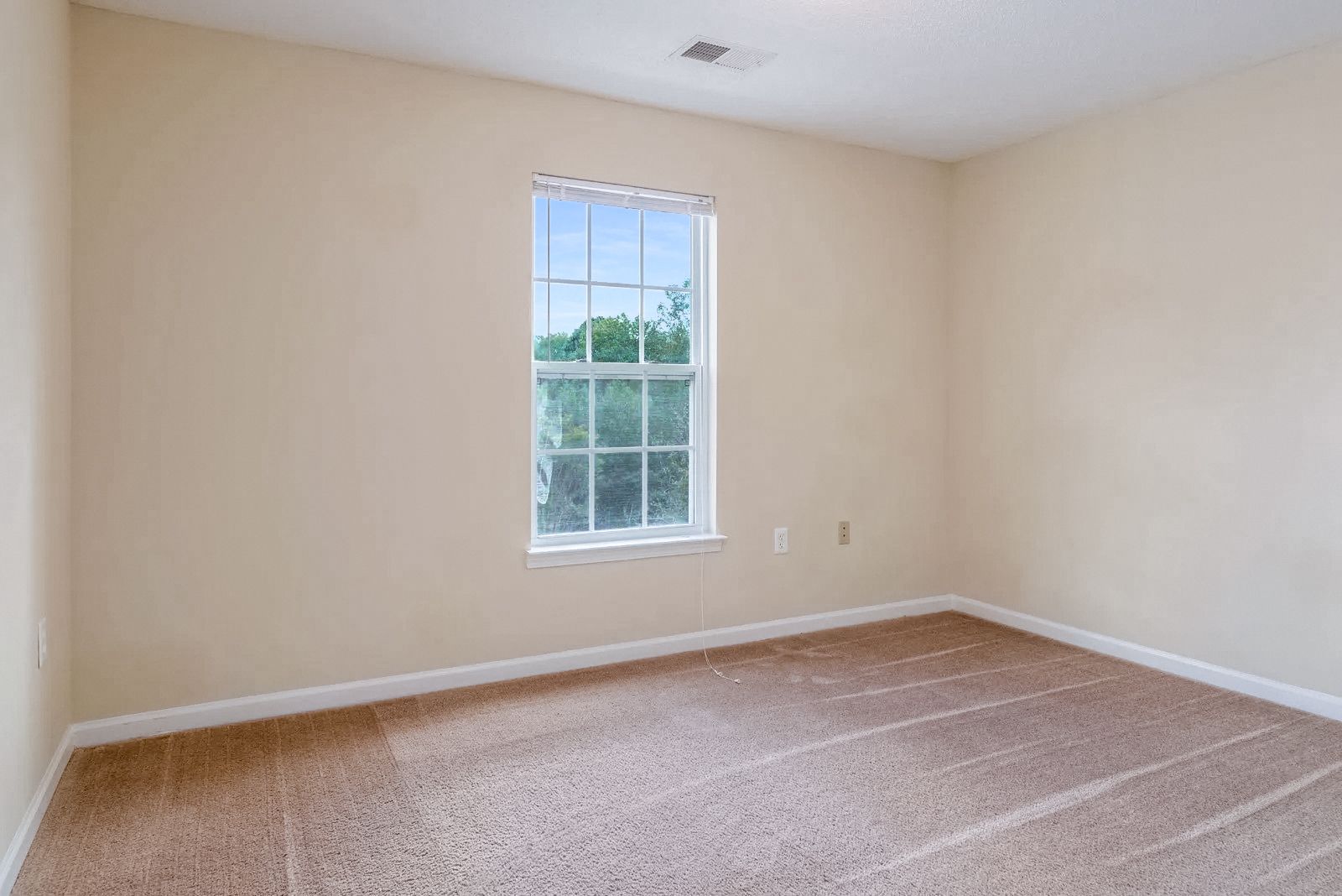 Empty room with beige walls, window, and brown carpet.