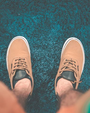 Person’s feet in tan sneakers standing on a blue textured floor.