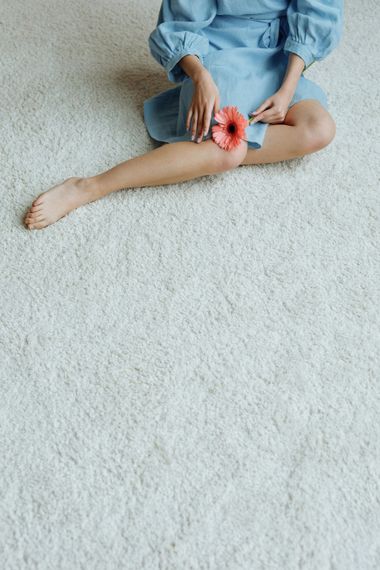 Person in a blue shirt applying a red bandage to a leg while sitting on a white carpet