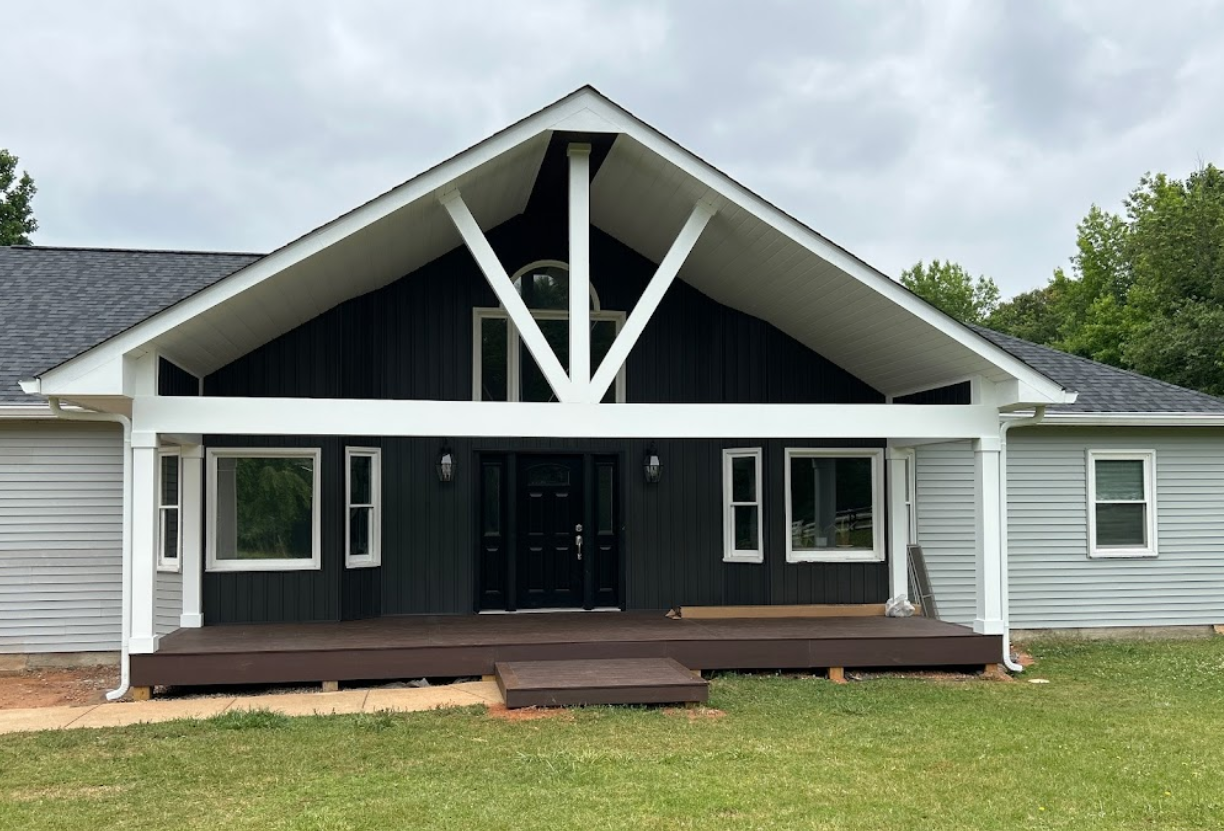 A black and white house with a porch and a roof.