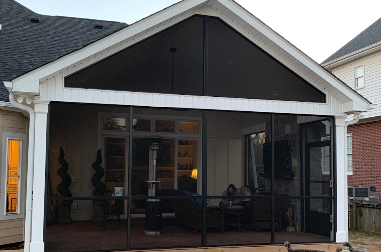 A screened in porch with a white house in the background.