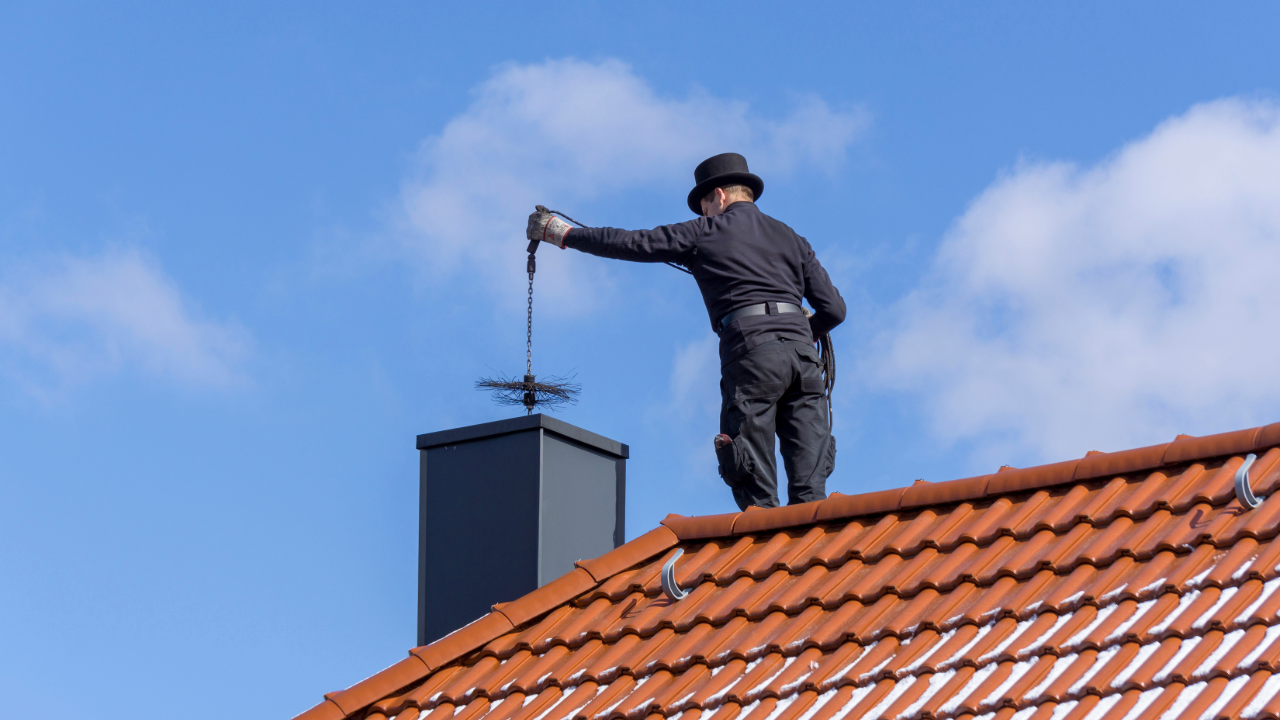 A man is standing on top of a roof holding a chimney sweeper.