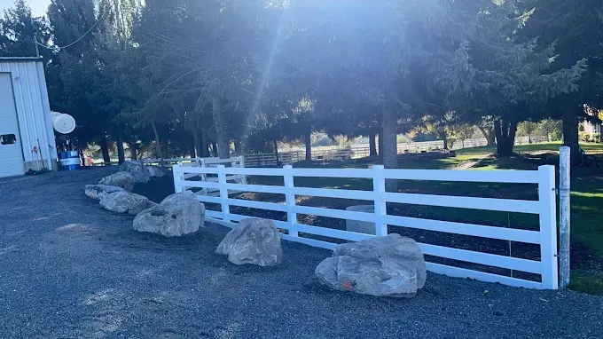 A white fence with rocks in front of it and trees in the background.