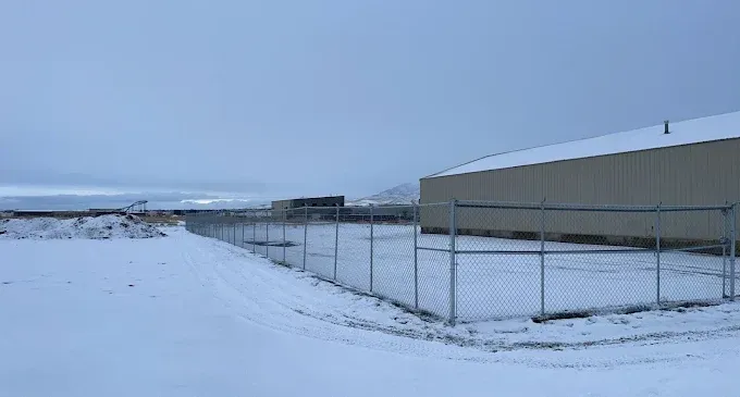 A chain link fence surrounds a snowy field with a building in the background.
