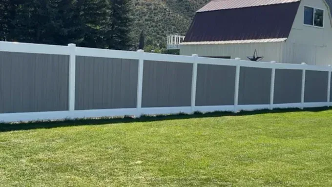 A white and gray fence surrounds a lush green lawn in front of a barn.