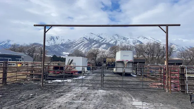 There is a gate in the middle of a dirt road with mountains in the background.