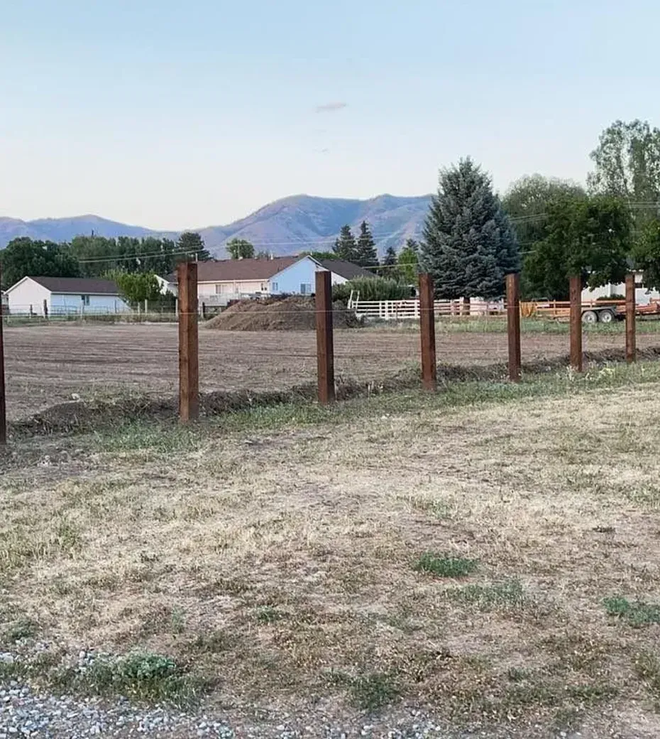 A wooden fence surrounds a dry grassy field with mountains in the background.