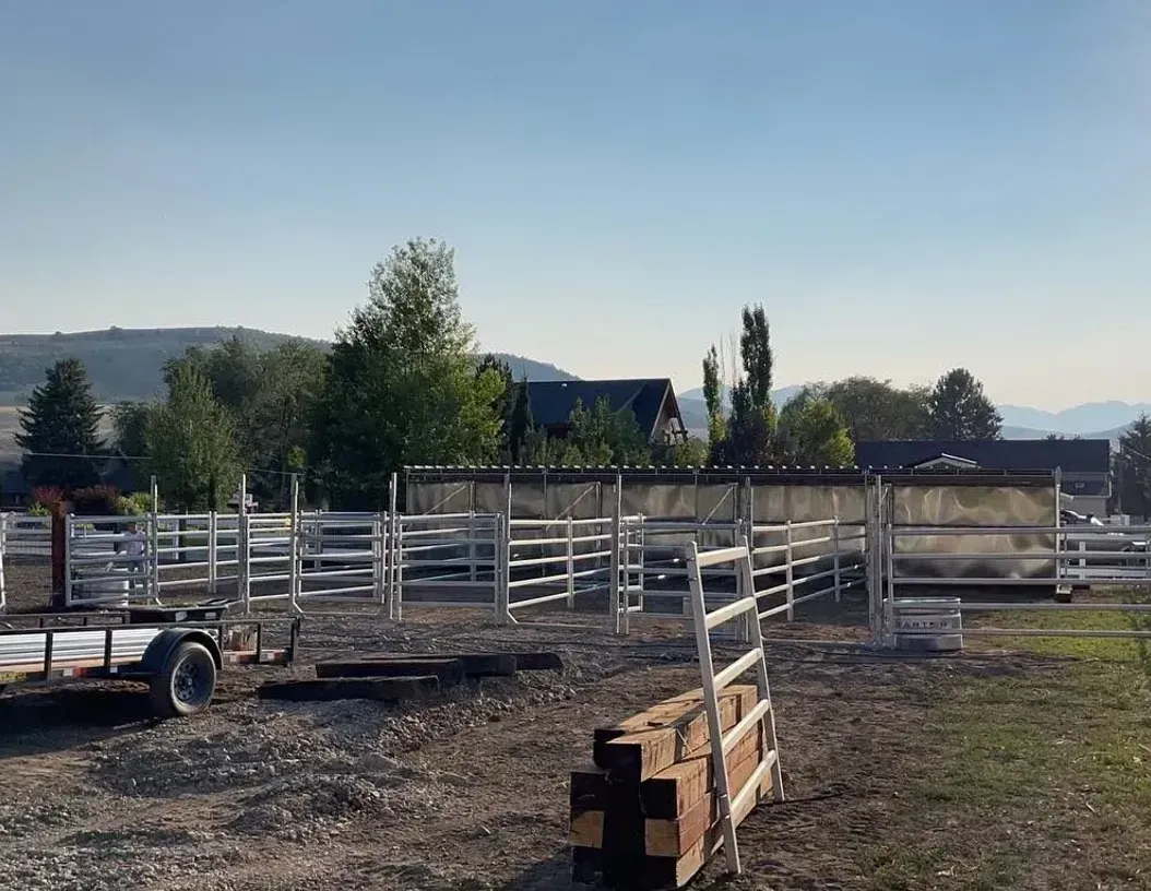 A dirt field with a lot of fences and trees in the background.