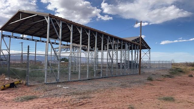 A wooden fence surrounds a dry grassy field with mountains in the background.
