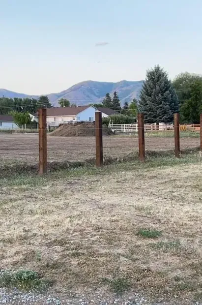 A wooden fence surrounds a dry grassy field with mountains in the background.