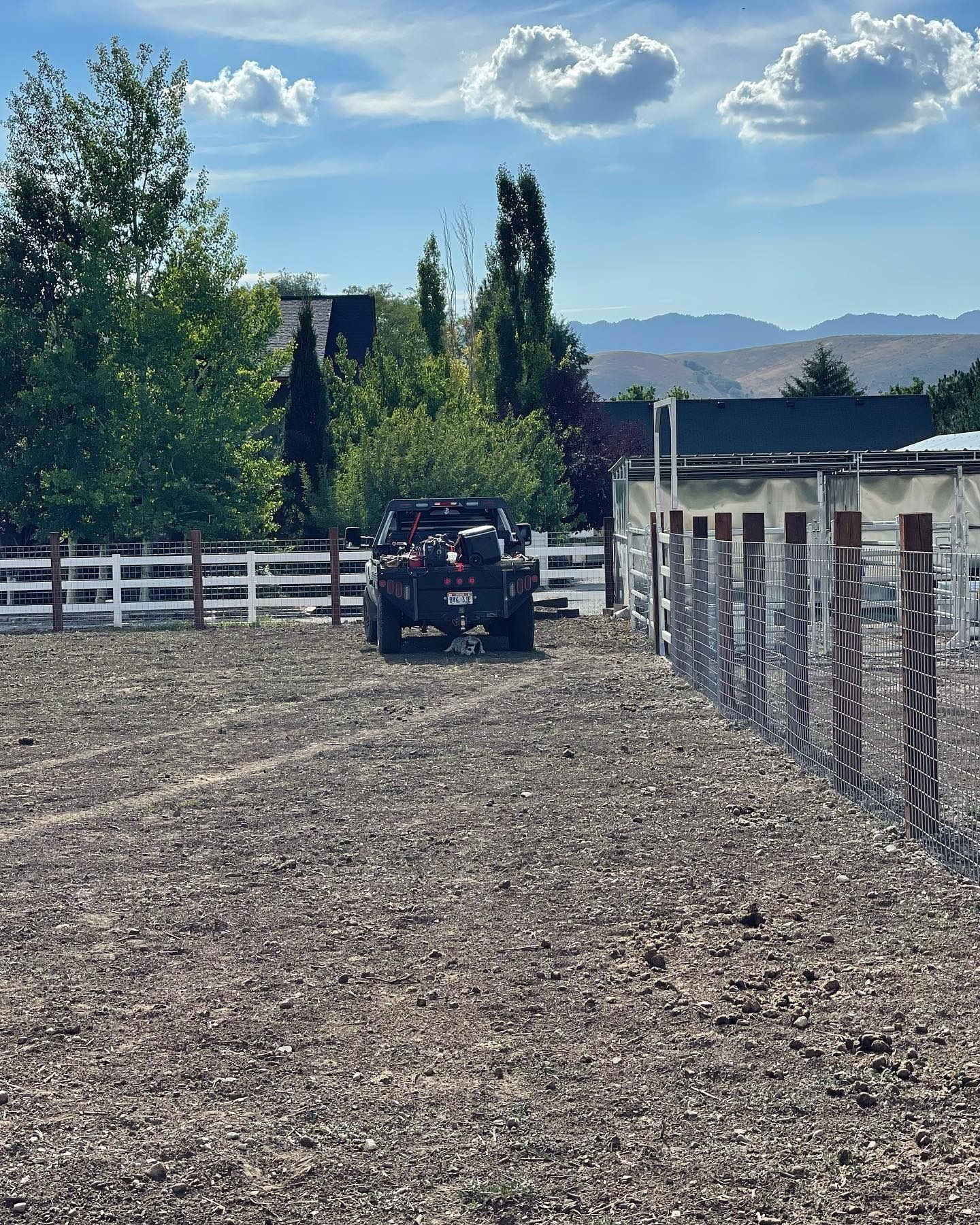 A truck is parked in a dirt field next to a fence.