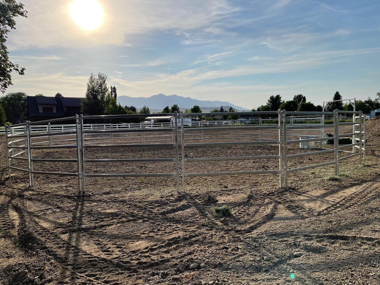 A fence surrounds a dirt field with mountains in the background