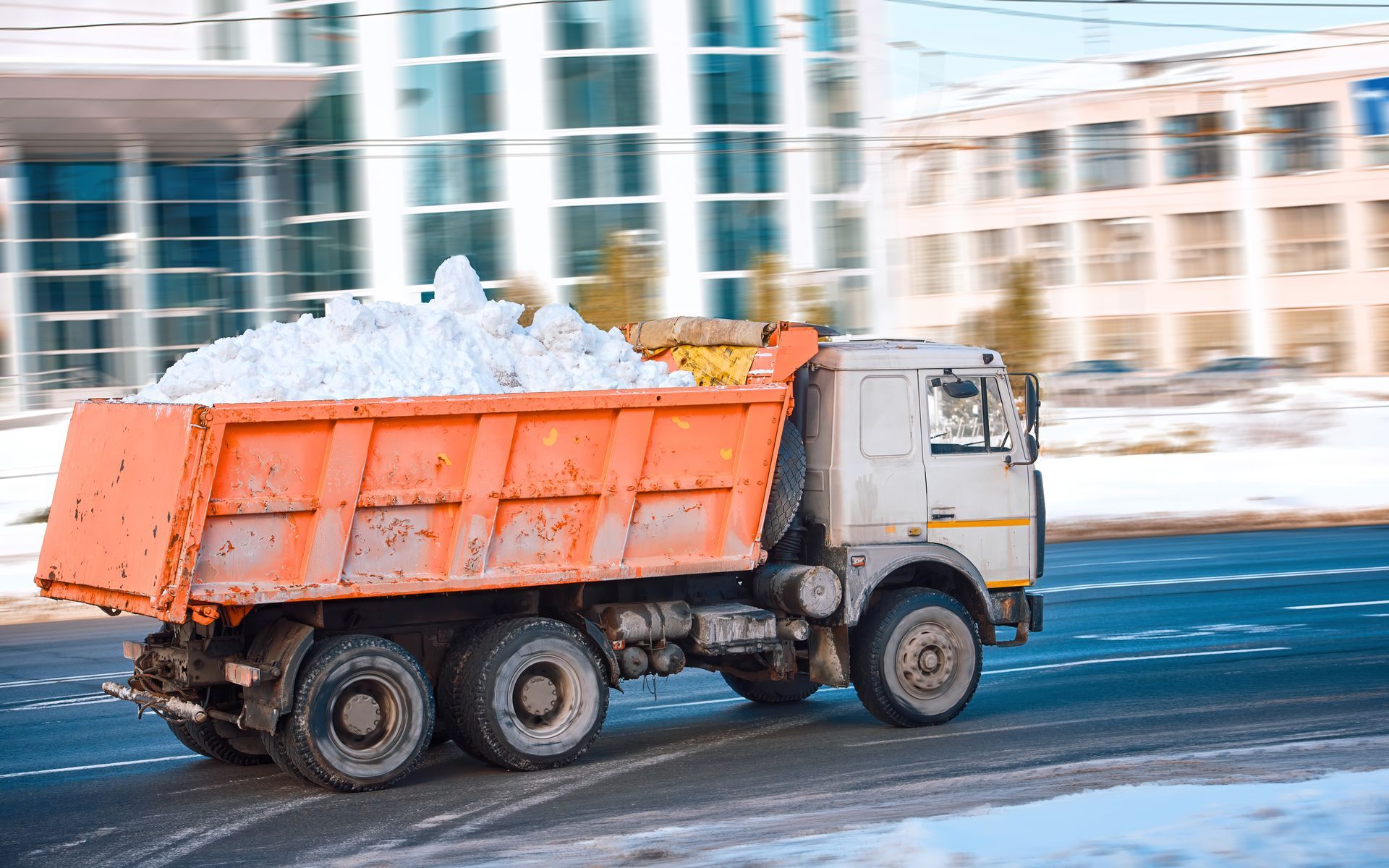 A dump truck filled with snow is driving down a city street.