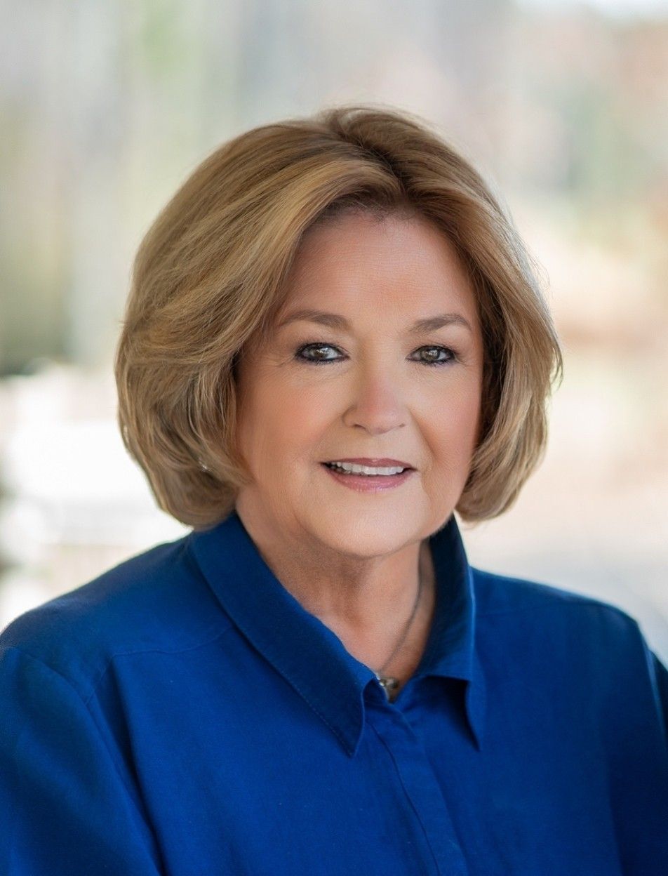 Woman with blonde hair and a blue shirt smiling at the camera against a blurred background.
