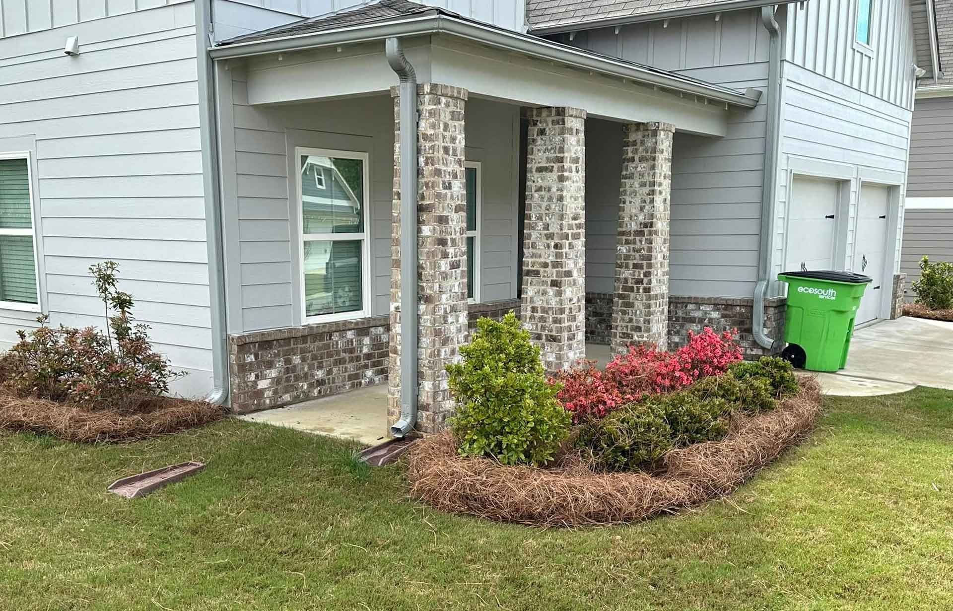 A house with a porch and a green trash can in front of it.